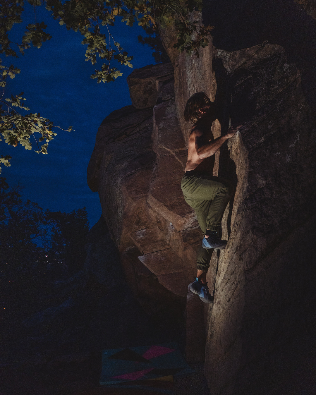 Climber on a vertical rock face beneath a deep blue evening sky.