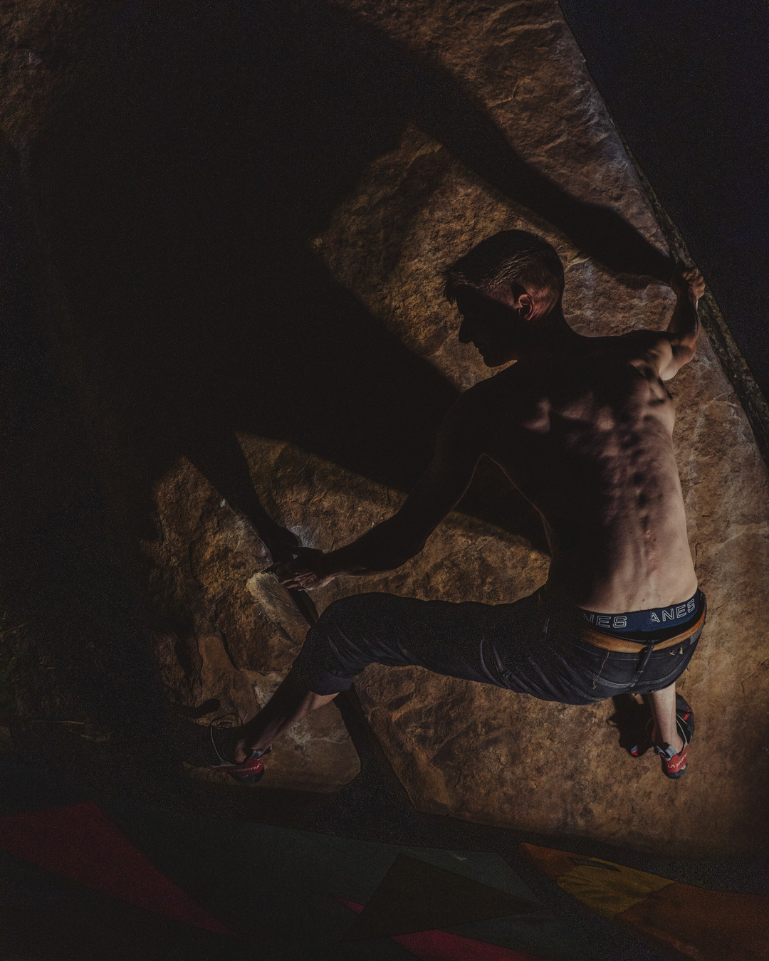 Climber reaching across a low overhanging boulder after dark.