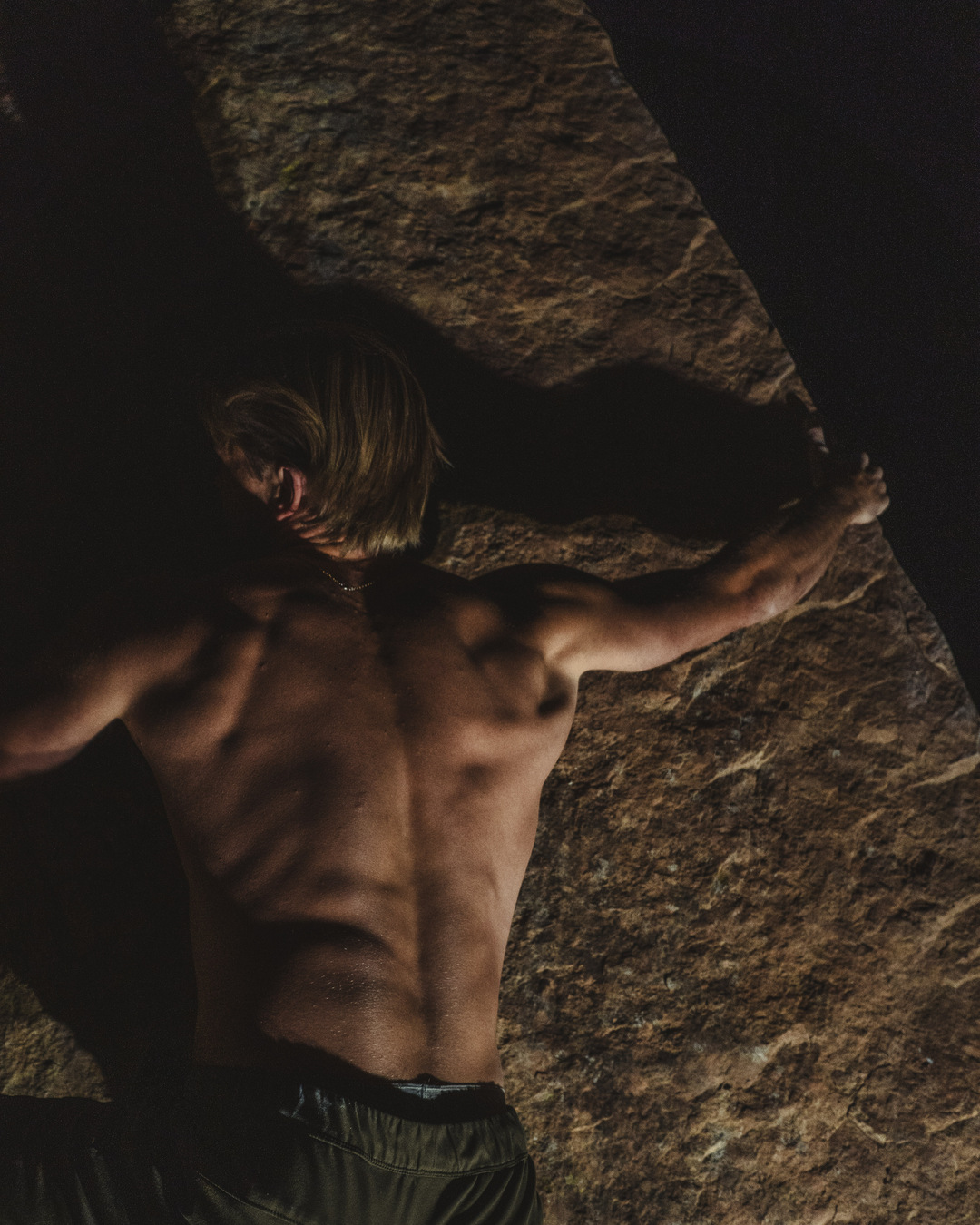 Close-up of a climber reaching across a warmly lit rock face.