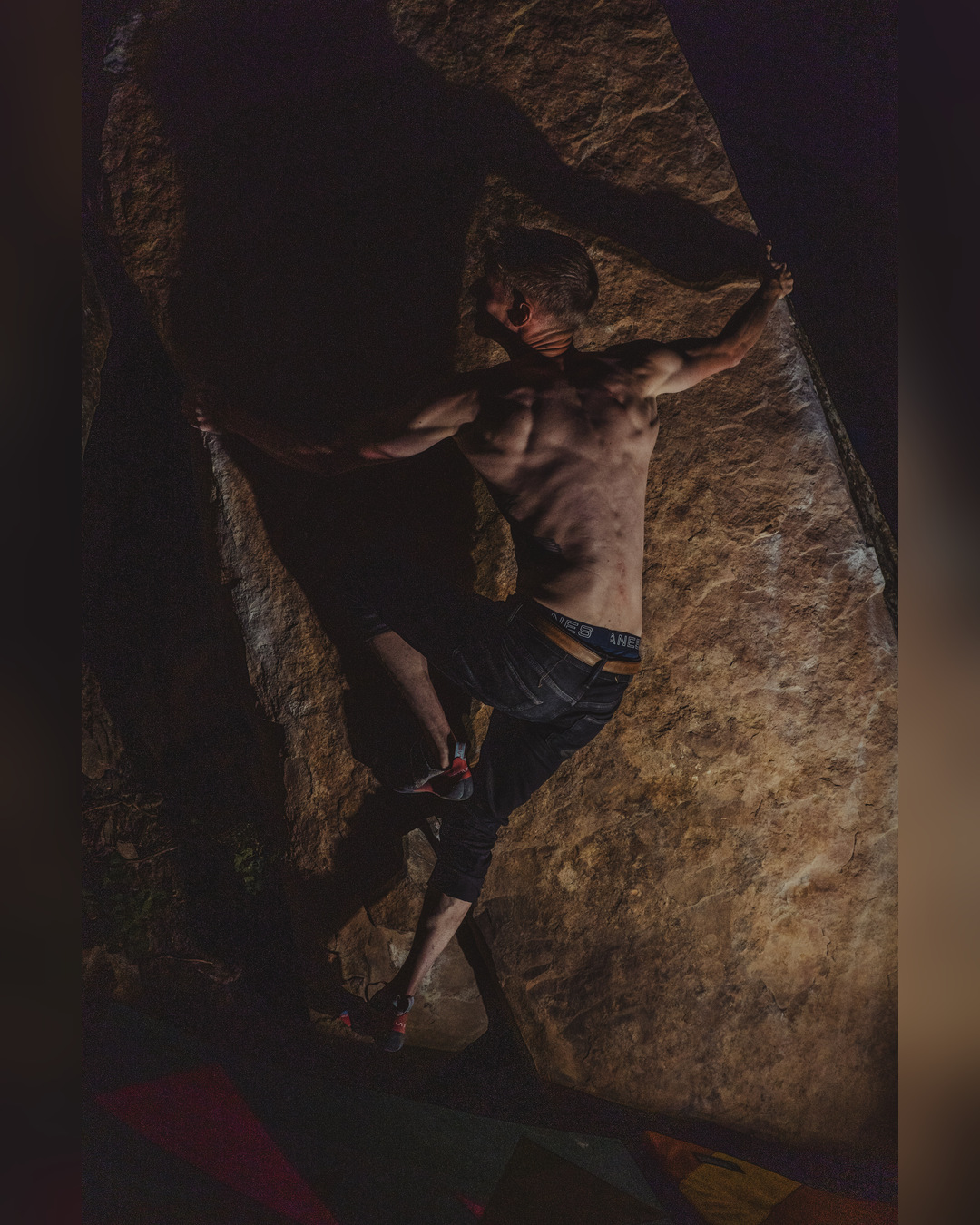 Climber moving across an overhanging boulder with one knee raised.