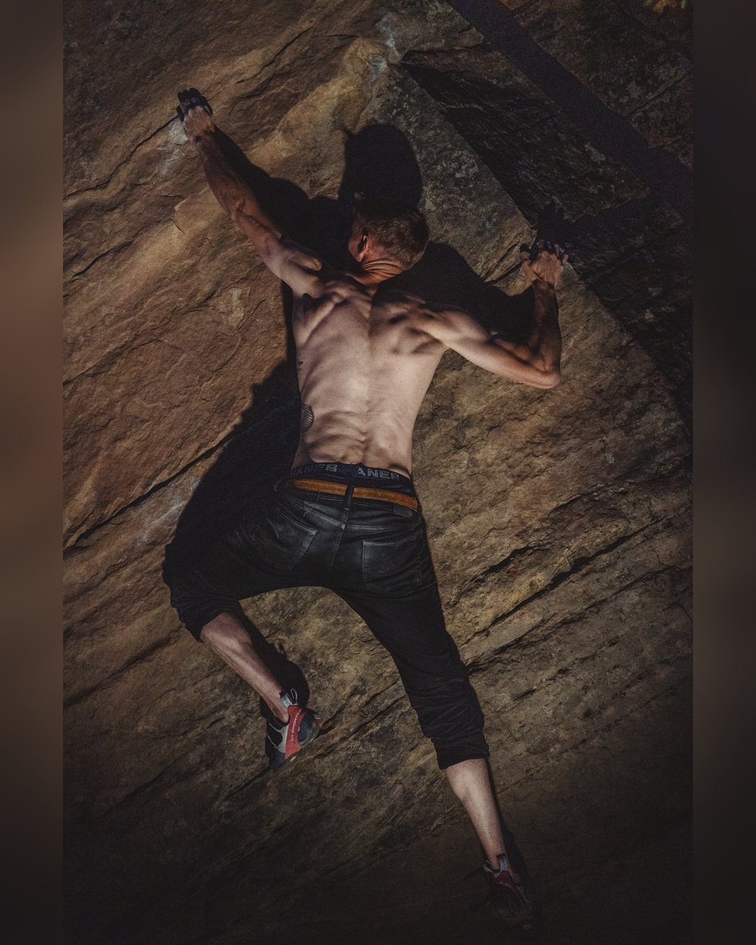 Climber stretching between holds on a steep rock face at night.
