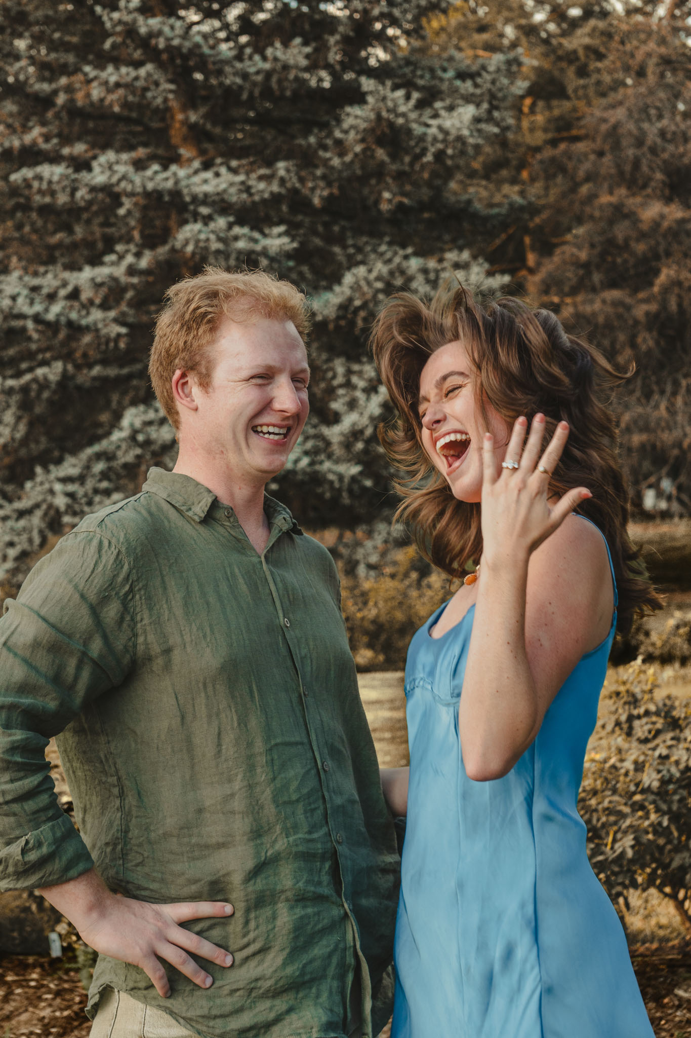 Couple laughing after a proposal, with the engagement ring held up.