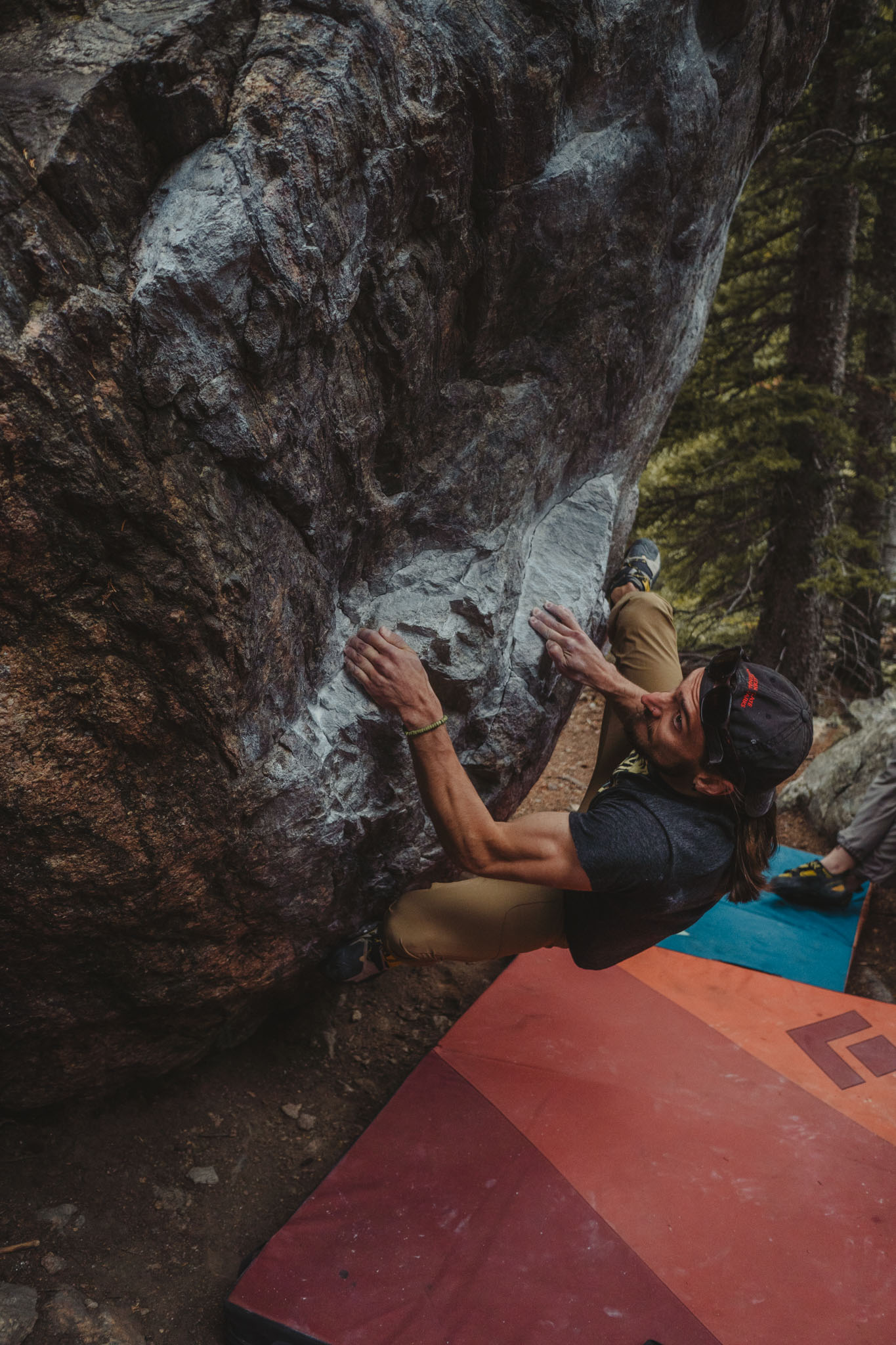 Climber holding an overhang above colorful bouldering crash pads.