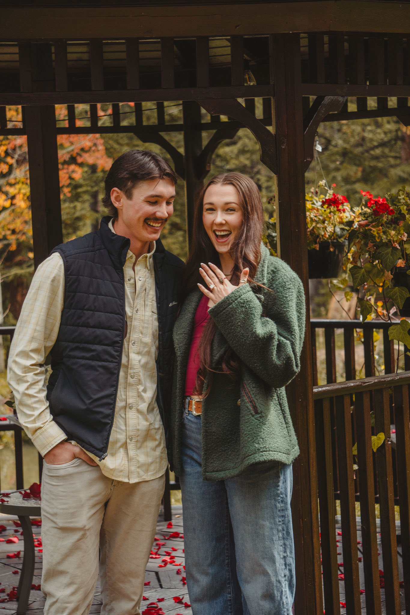 Couple laughing together as an engagement ring is shown beside a gazebo.