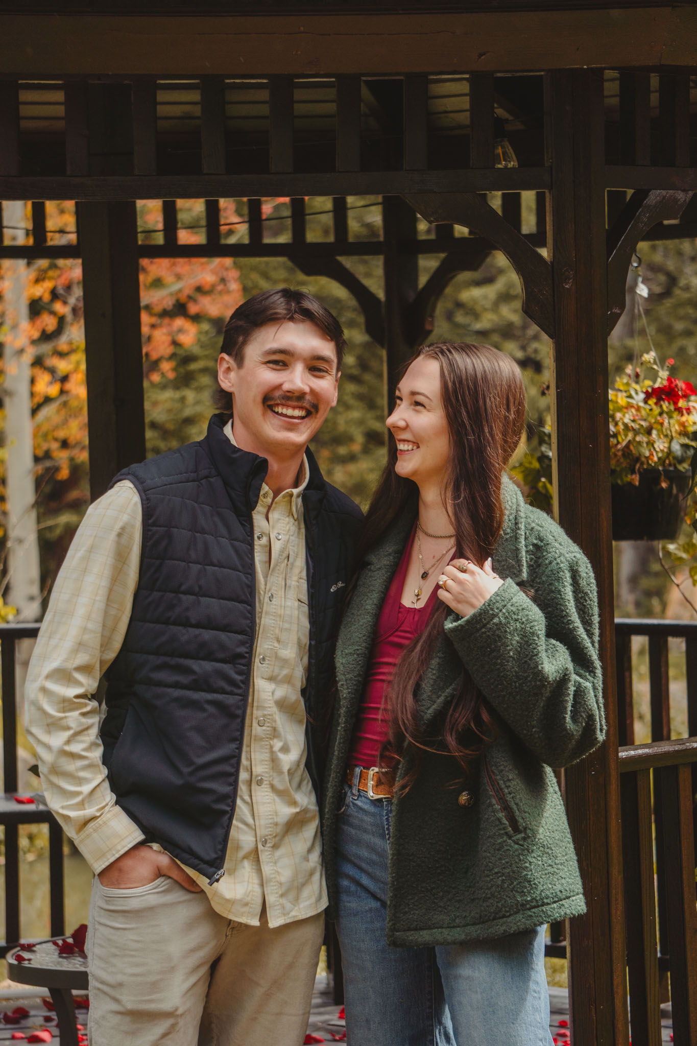 Couple sharing smiles in a rustic gazebo surrounded by fall foliage.