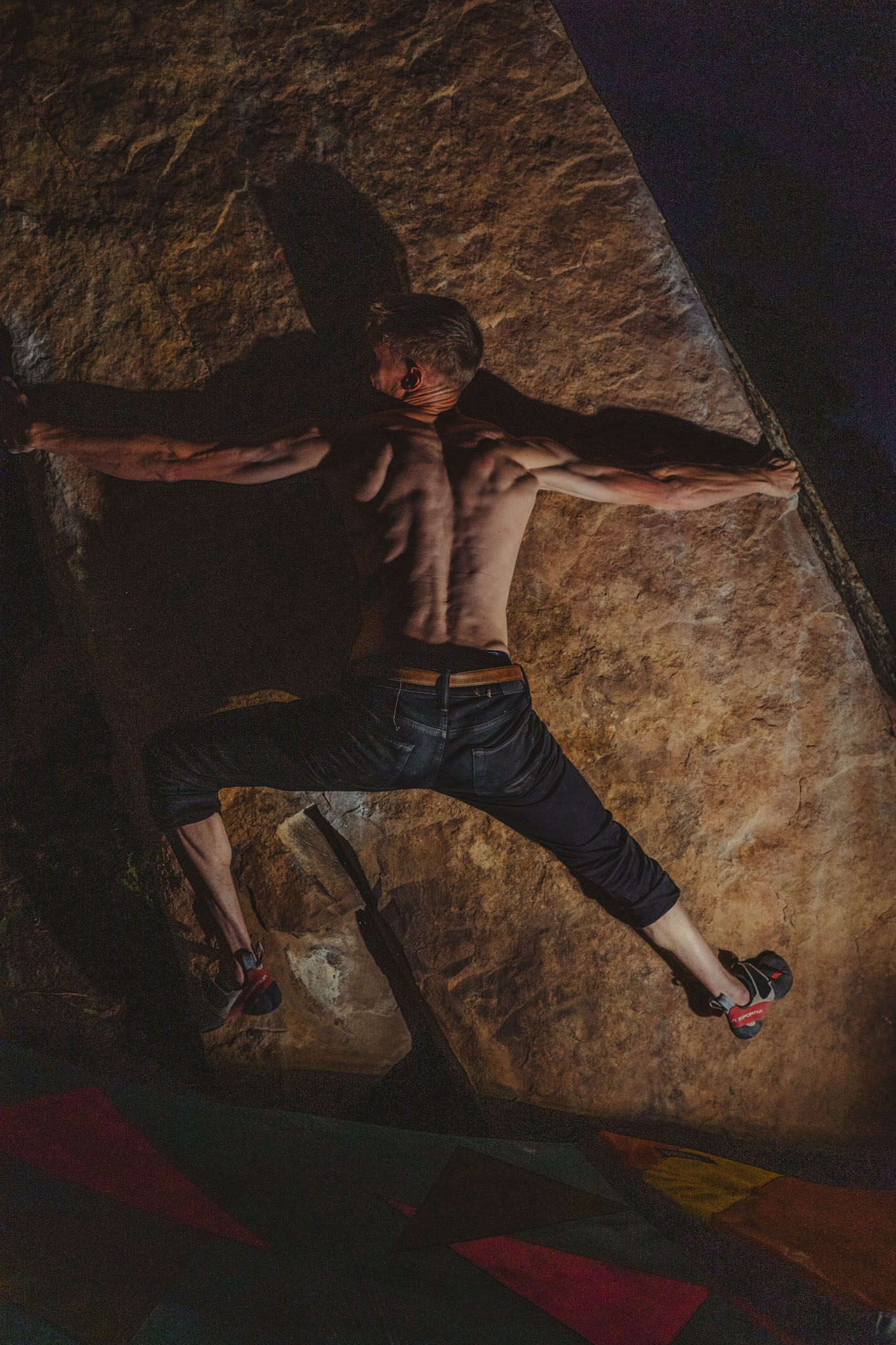 Climber stretched across a boulder under warm light at night.