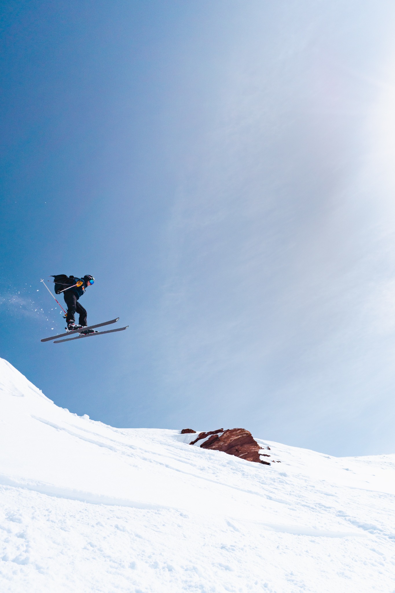 Skier airborne above a steep snowy ridge beneath open blue sky.