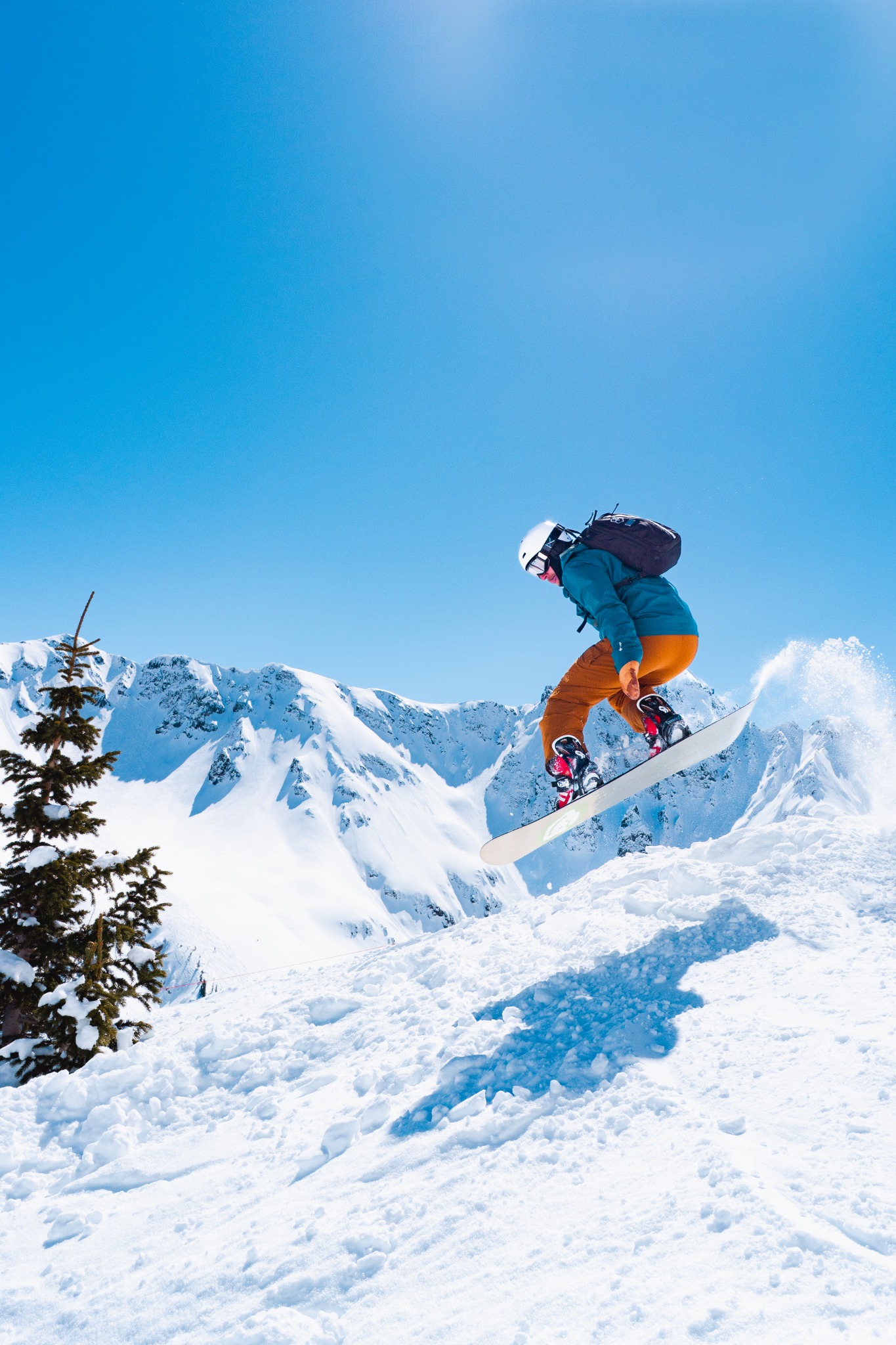 Snowboarder jumping with snow-covered mountain peaks in the background.