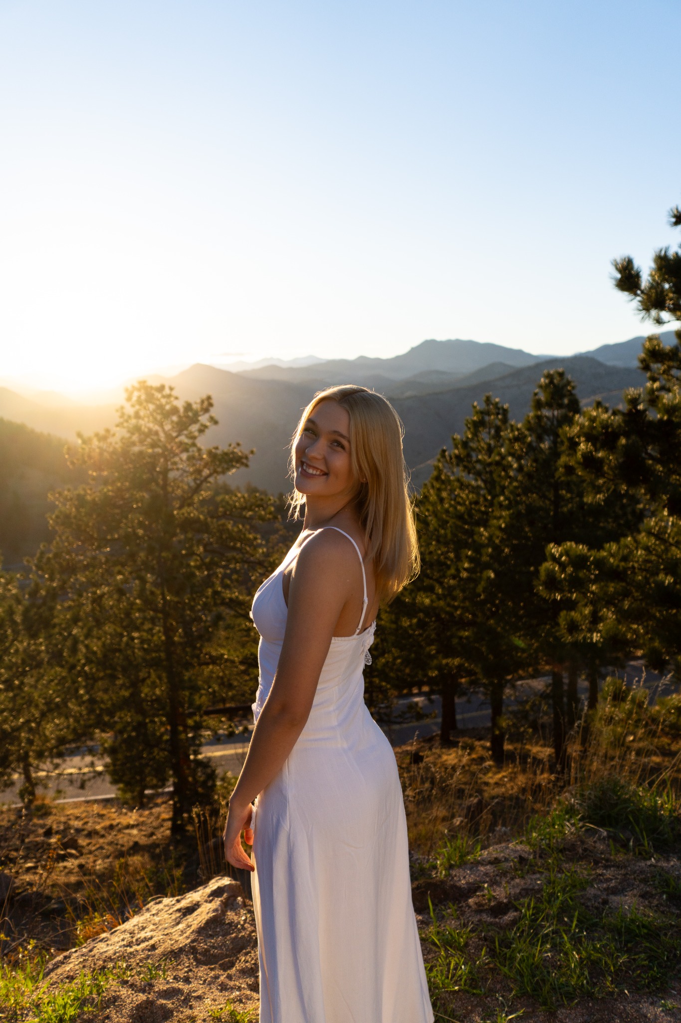 Portrait in a white dress overlooking mountain ridges at sunset.