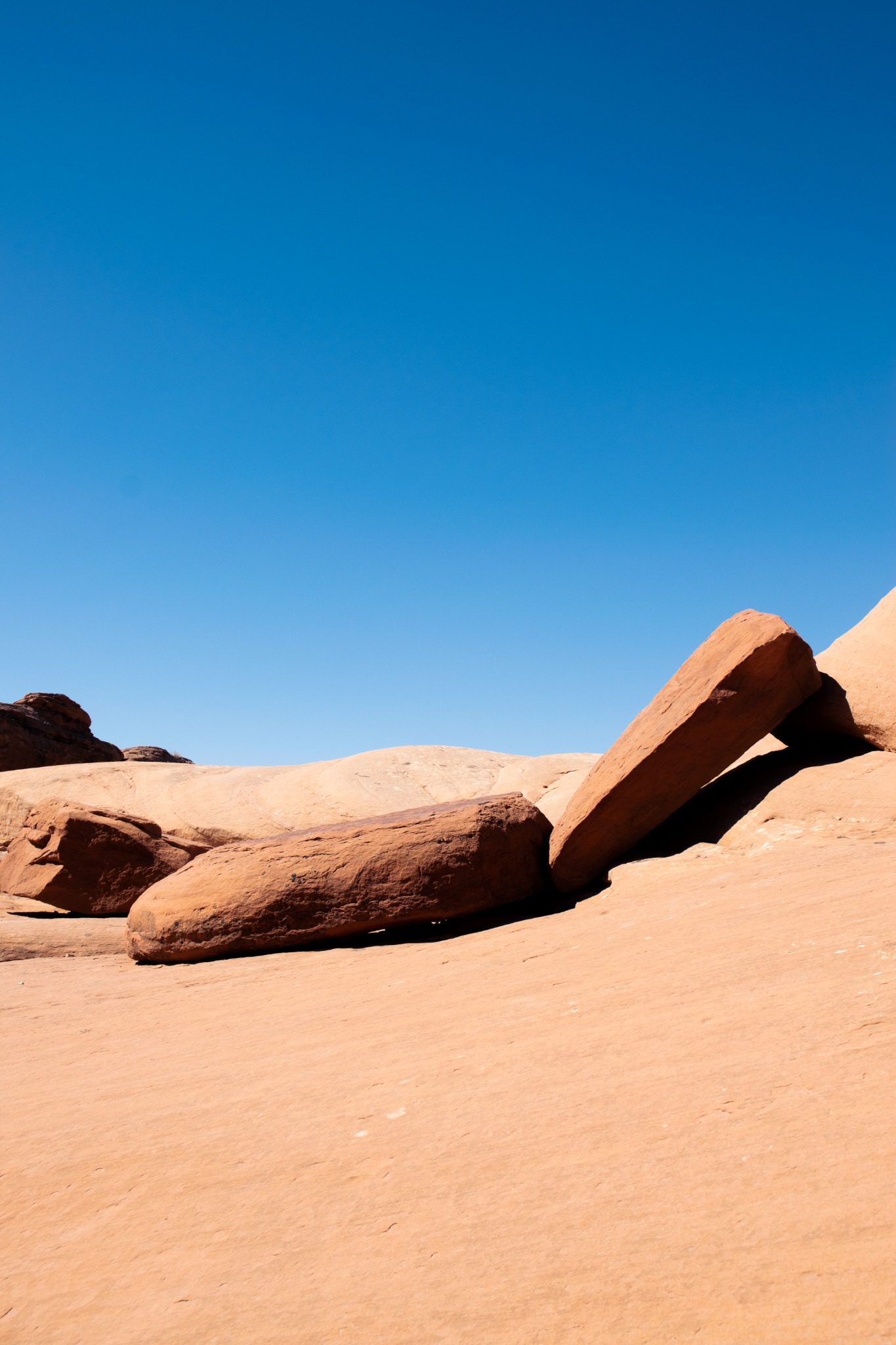 Angular orange sandstone slabs casting deep shadows across smooth rock beneath a clear blue sky.